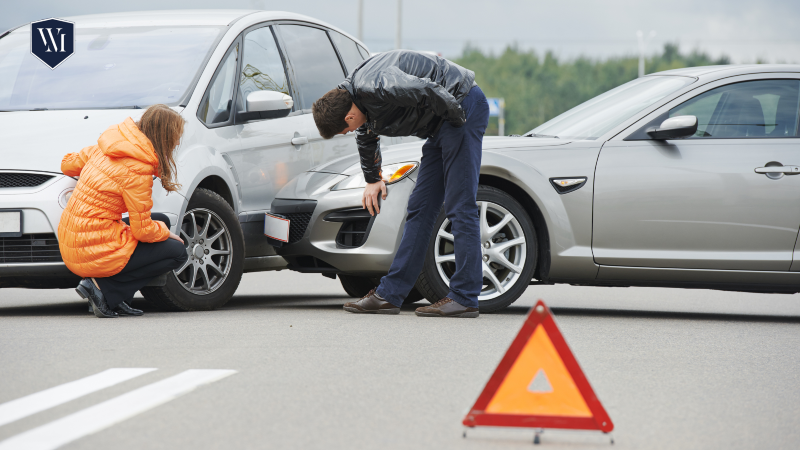 Personas inspeccionando daños en vehículos después de un choque en carretera con triángulo de advertencia visible, ilustrando un caso típico que manejan los abogados de accidentes de Whittel & Melton.